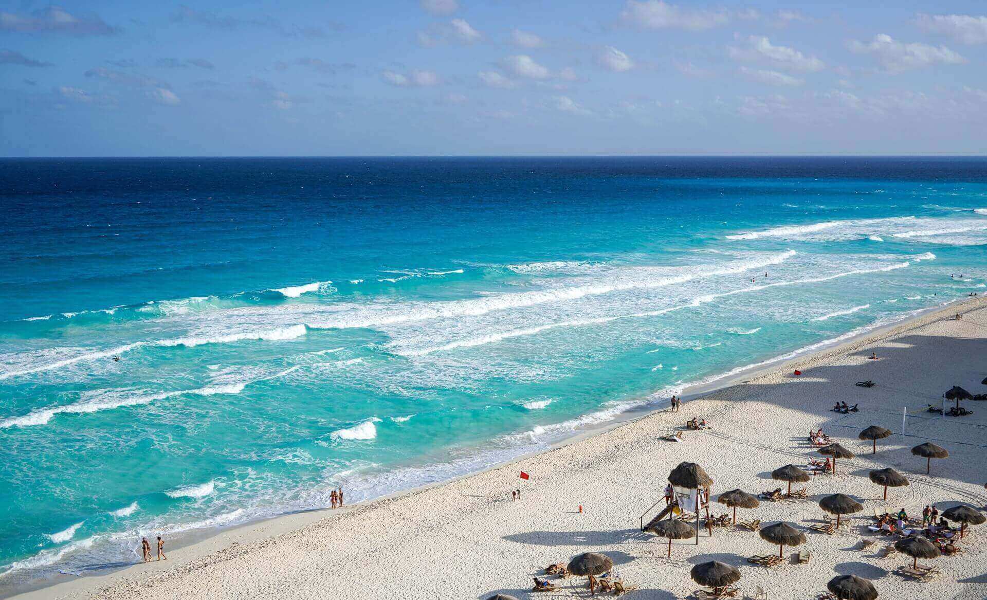 Sweeping view of Cancun's turquoise waters and white-sand beach lined with sun loungers and umbrellas. 