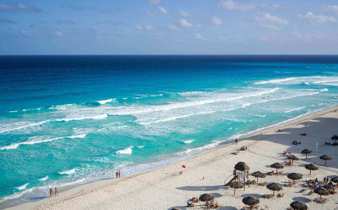 Sweeping view of Cancun's turquoise waters and white-sand beach lined with sun loungers and umbrellas. 