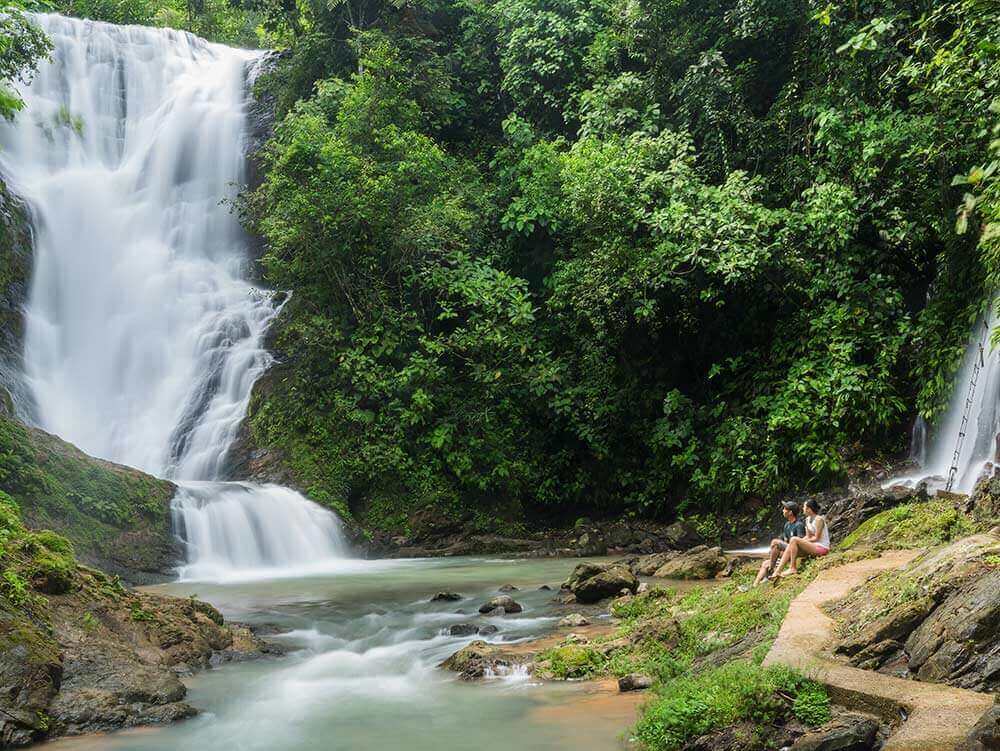 A couple enjoys the view at Los Campesinos Waterfall, where tiers of water cascade through lush Costa Rican rainforest. 
