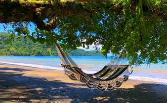 A hammock sways in the shade, overlooking the tranquil beach and turquoise waters of Playa Cativo. 