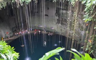 Visitors swim in the natural waters of Cenote Ik Kil, surrounded by hanging vines and limestone walls in Yucatan, Mexico. 