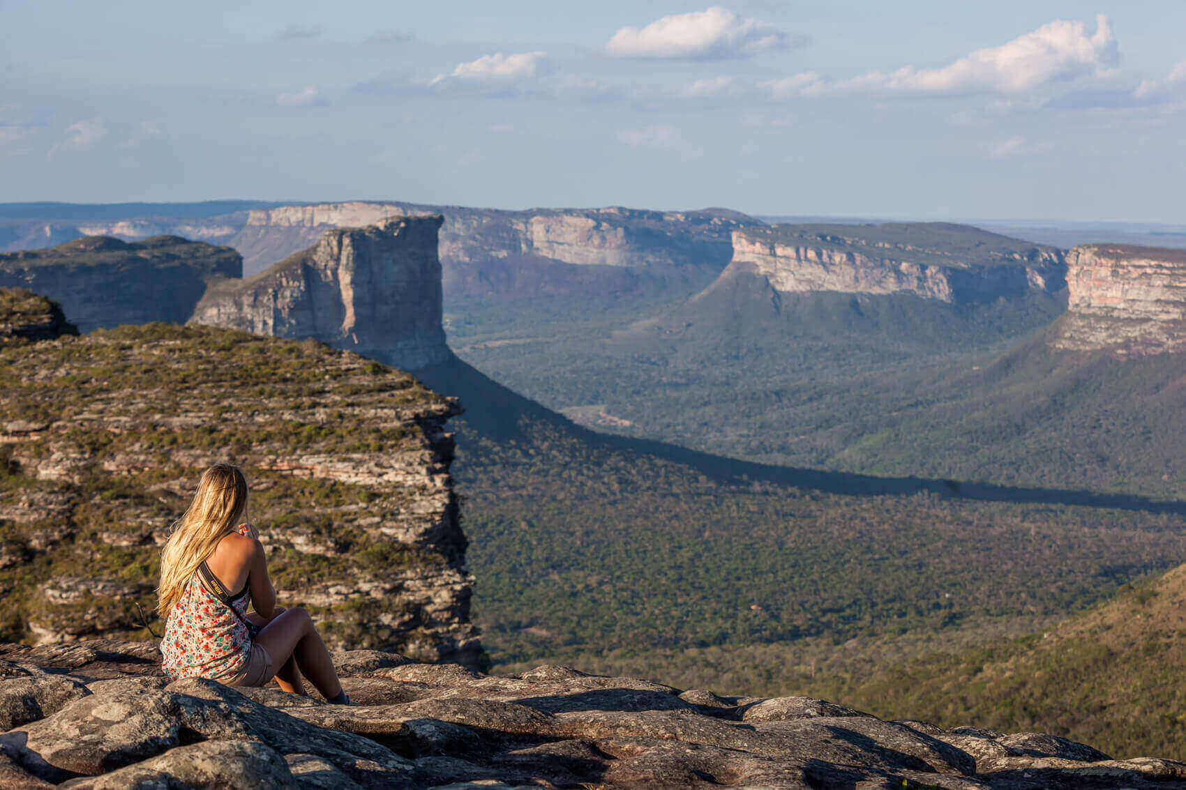 Woman sitting on cliff edge with panoramic views of mountains in Chapada Diamantina National Park, Brazil. 