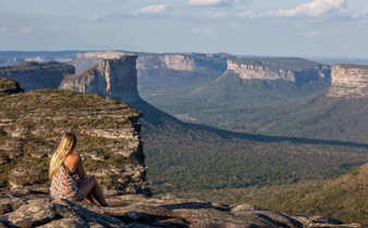 Woman sitting on cliff edge with panoramic views of mountains in Chapada Diamantina National Park, Brazil. 