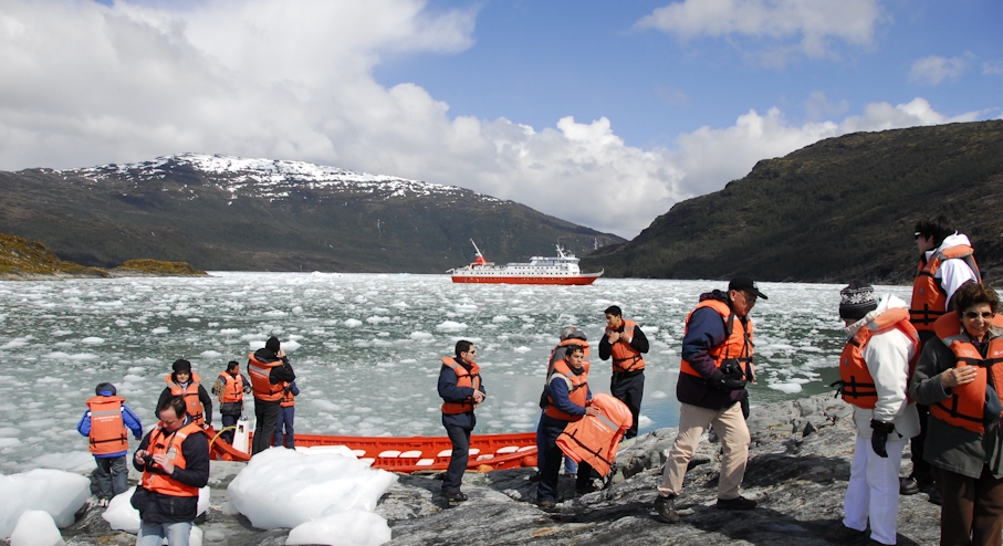 Tourists in life jackets disembark from Zodiacs onto an icy shoreline during a glacier expedition cruise in Chilean Patagonia. 