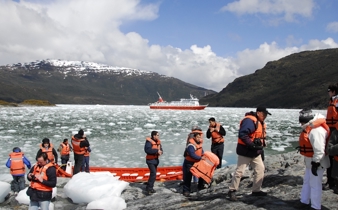 Tourists in life jackets disembark from Zodiacs onto an icy shoreline during a glacier expedition cruise in Chilean Patagonia. 