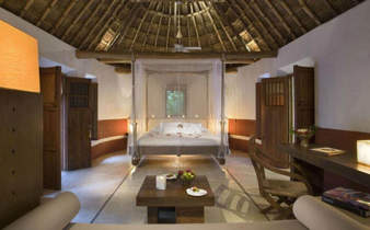 Spacious interior of a luxury Mayan-style villa with palapa roof, canopy bed, and natural wood furnishings in Mexico. 