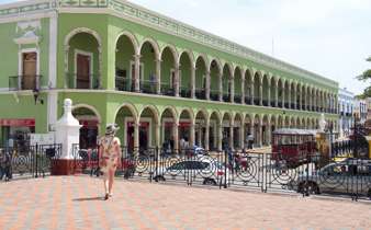 Historic green arcade building on Merida's Plaza Grande, Yucatan, with colonial arches, statue, and pedestrian view. 