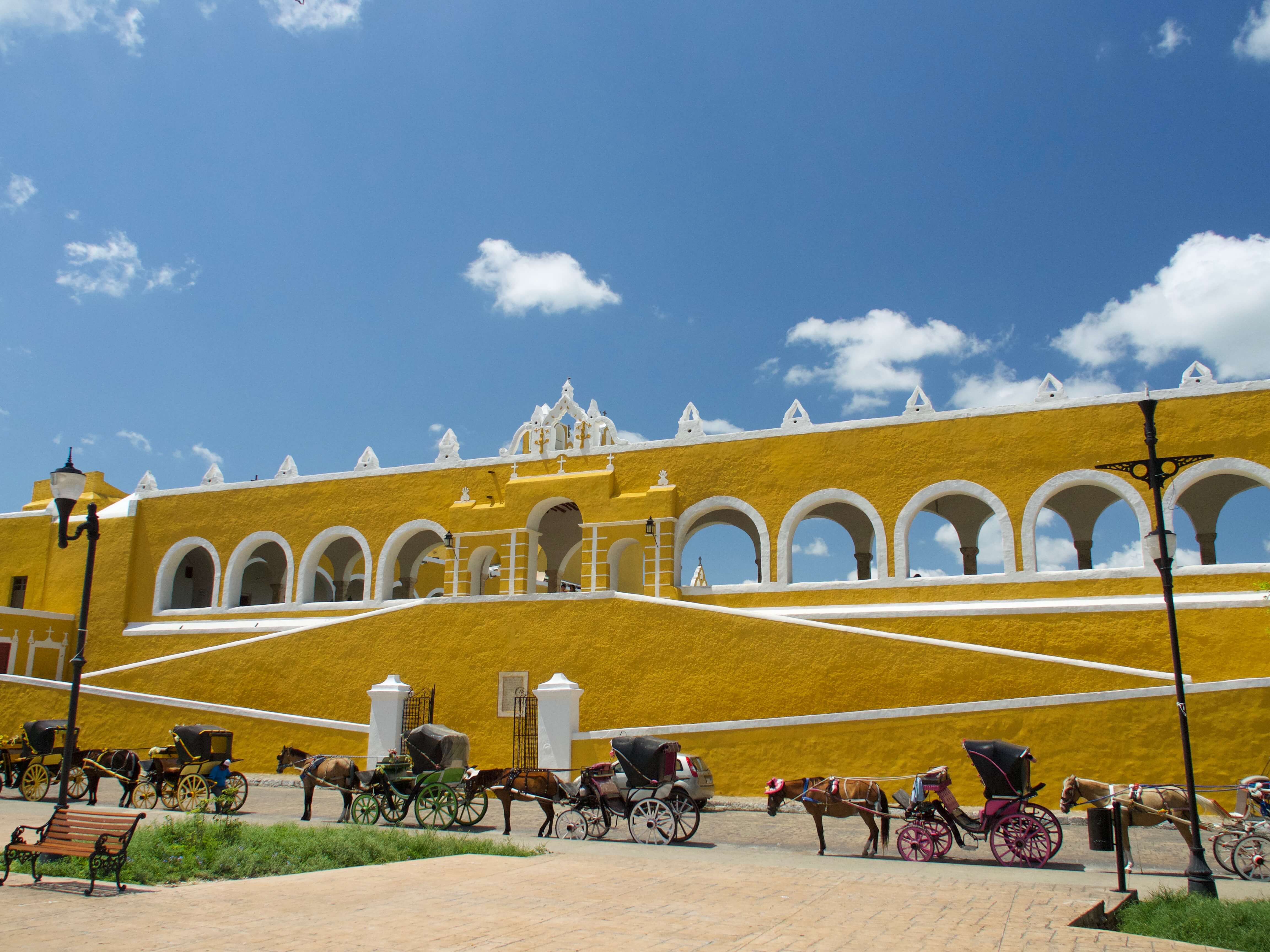 Horse-drawn carriages line the front of the bright yellow Convent of San Antonio de Padua in Izamal, Yucatan, Mexico. 