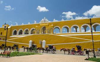 Horse-drawn carriages line the front of the bright yellow Convent of San Antonio de Padua in Izamal, Yucatan, Mexico. 