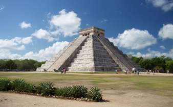 The Temple of Kukulcan at Chichen Itza rises under a bright sky, showcasing ancient Mayan architectural brilliance. 