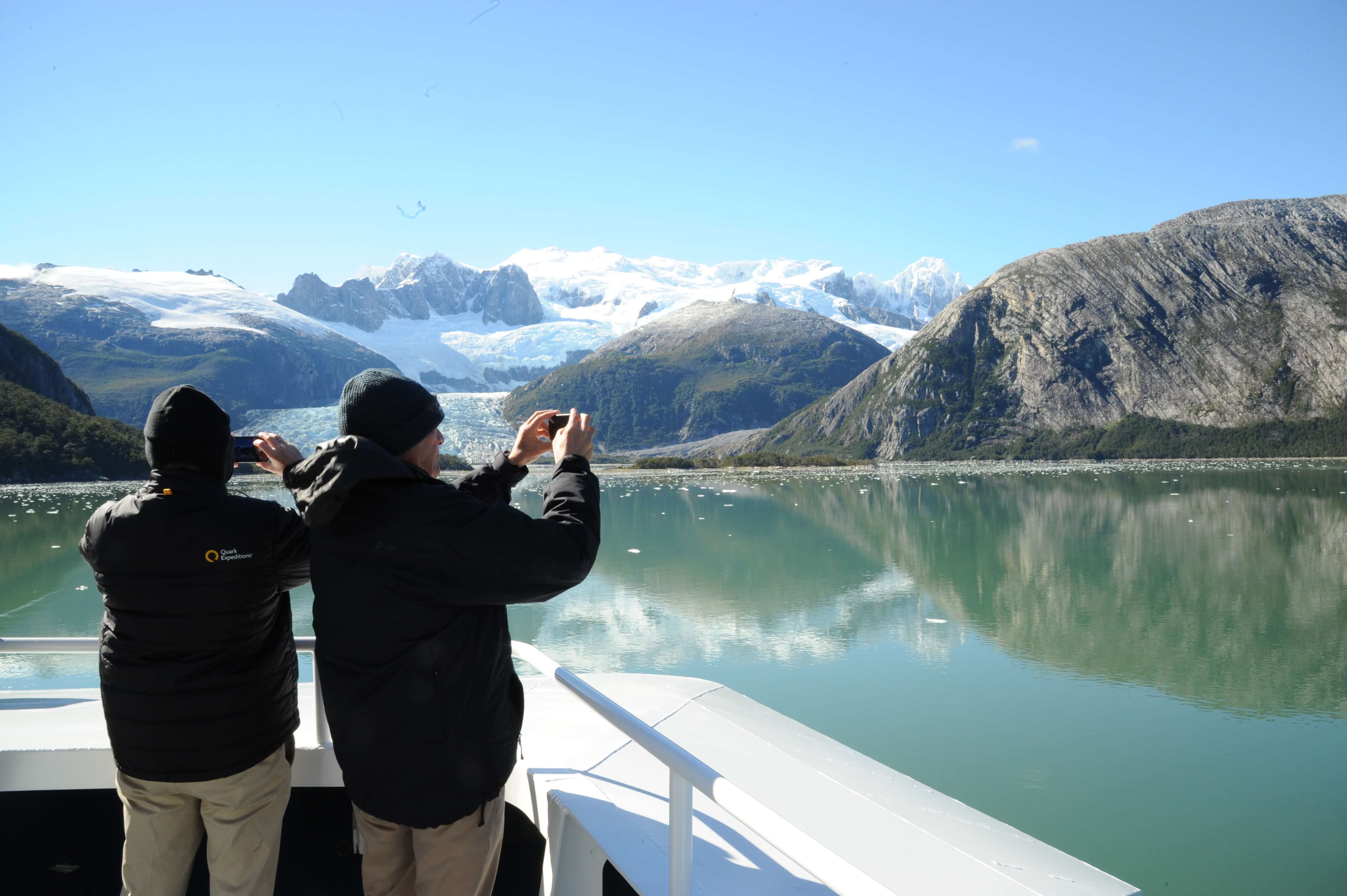 Two passengers photograph stunning glaciers and snow-capped peaks from the deck of a cruise ship in Chilean Patagonia. 