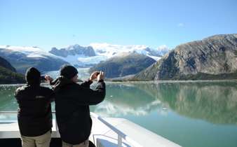 Two passengers photograph stunning glaciers and snow-capped peaks from the deck of a cruise ship in Chilean Patagonia. 