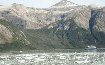 An expedition cruise ship navigates icy Patagonia waters beneath towering, rugged mountains in Chile's southern fjords. 