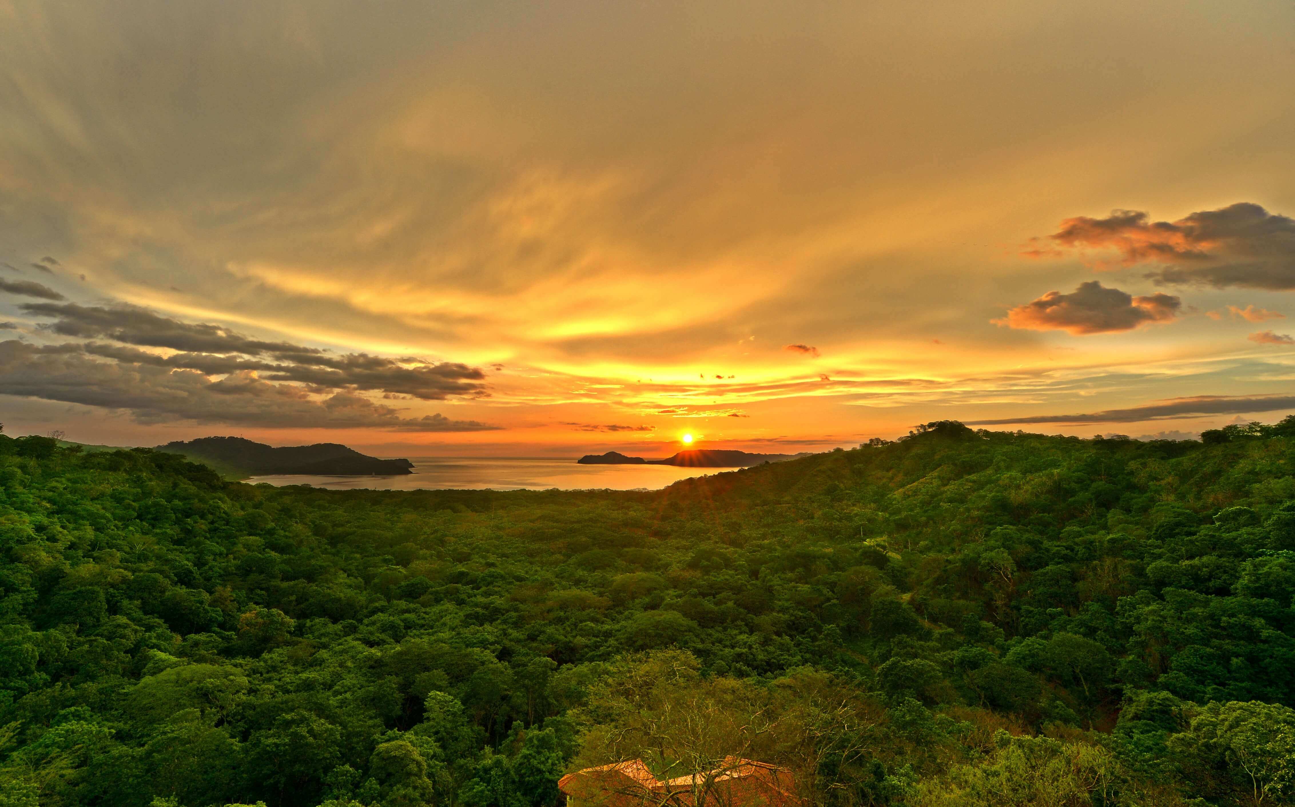 Golden sunset over the forested hills of Guanacaste, with the sun setting above the Pacific horizon. 