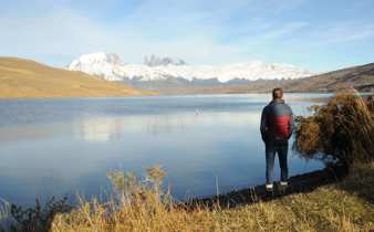 A lone visitor stands beside a still lake reflecting snow-capped peaks in Chile's Torres del Paine National Park. 