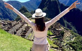 Woman with arms raised overlooking Machu Picchu and the Andes Mountains Peru. 