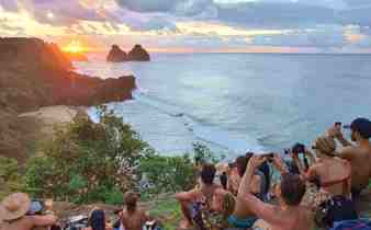 Tourists gathered at sunset viewpoint overlooking the ocean and Morro Dois Irmaos rocks in Fernando de Noronha, Brazil. 