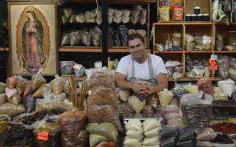 Friendly vendor in San Miguel de Allende sits among sacks of grains and spices, under the gaze of the Virgin of Guadalupe. 