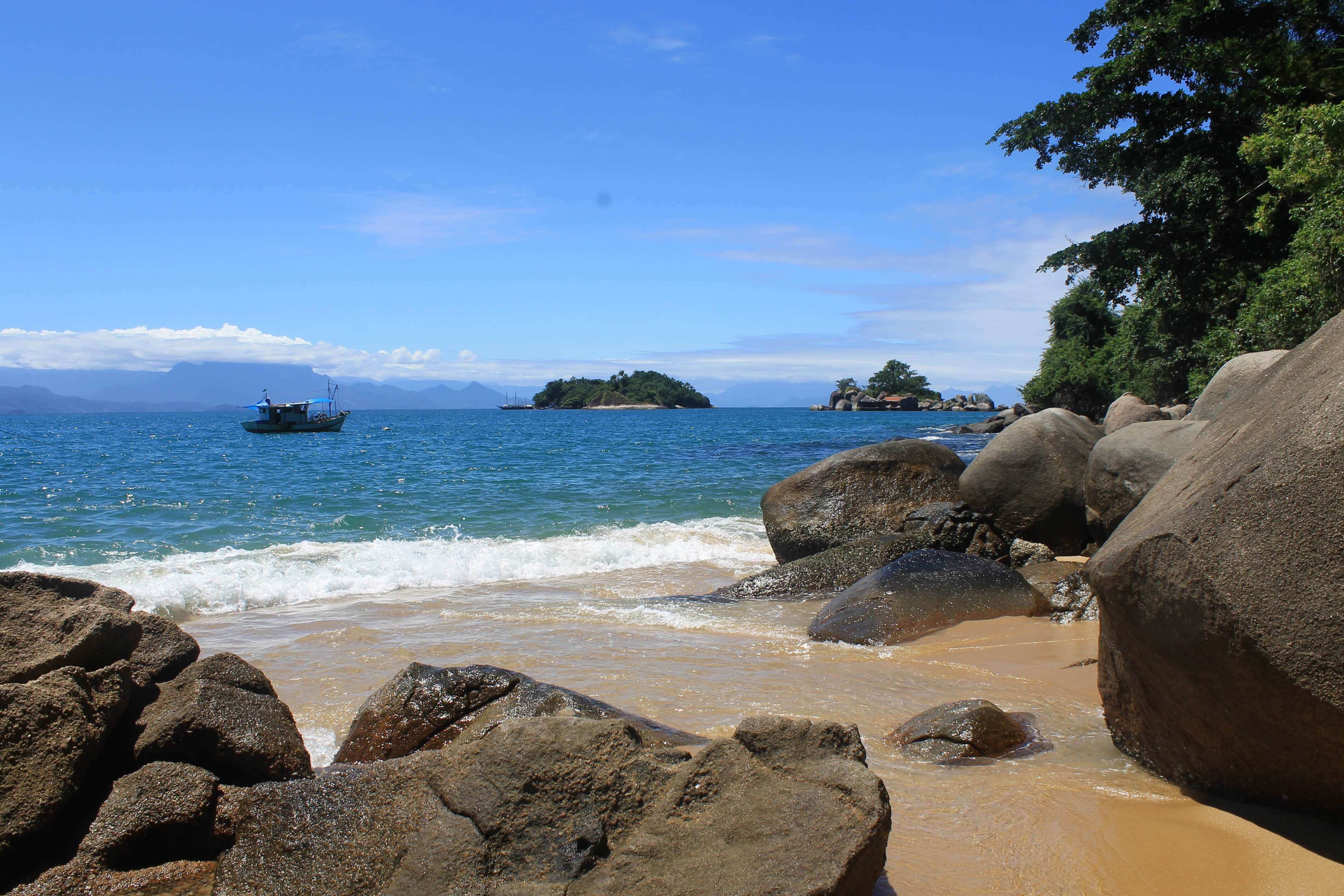 Small boat anchored off a secluded beach with rocky shoreline on Ilha Grande. 