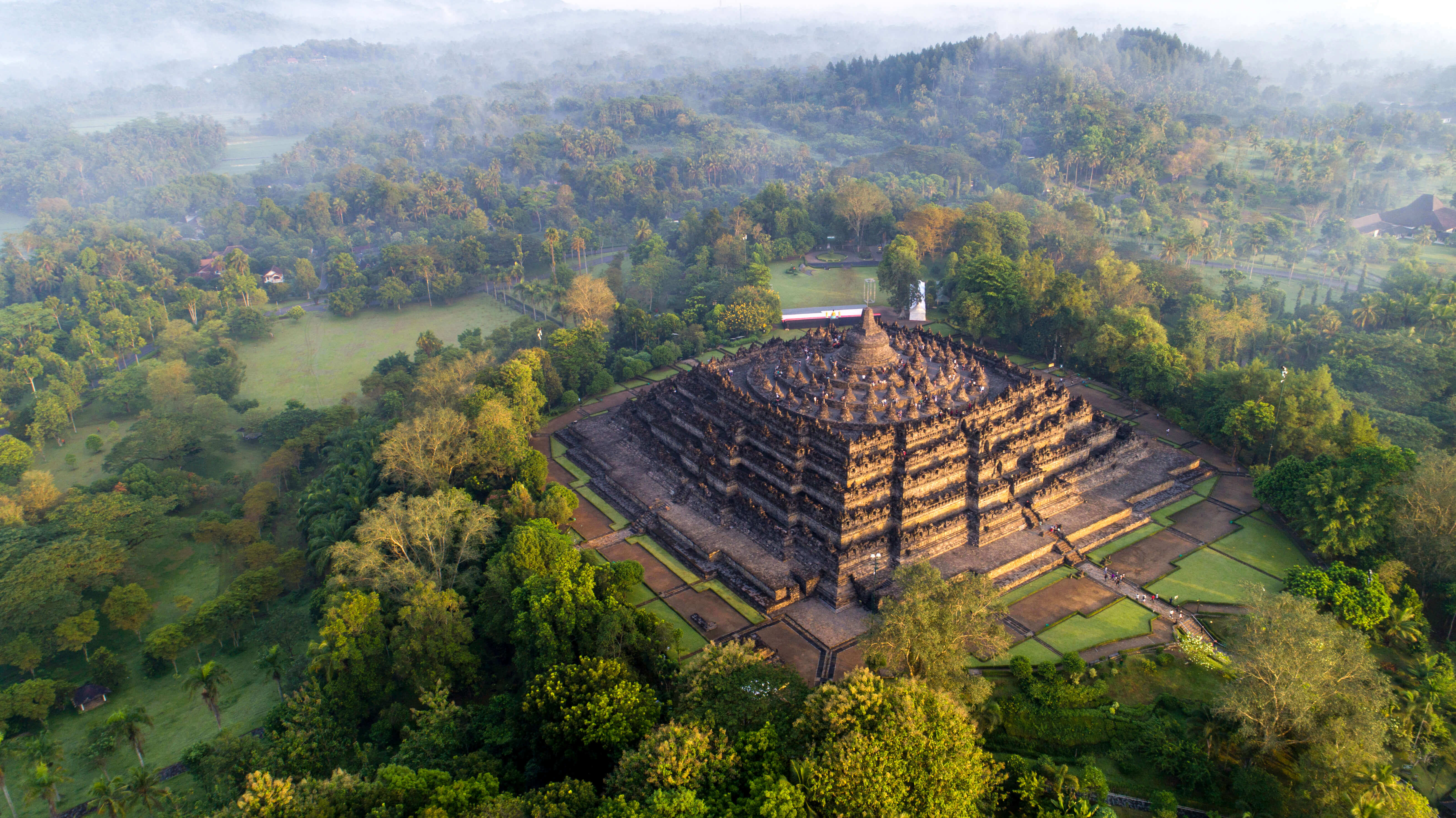 An aerial view of Borobudur Temple surrounded by misty forest in Central Java, Indonesia at sunrise. 