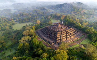 An aerial view of Borobudur Temple surrounded by misty forest in Central Java, Indonesia at sunrise. 